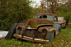 Sitting in a field are 2 old rusted cars. 