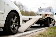 Picture of a car getting towed by a flatbed truck on the side of a road.