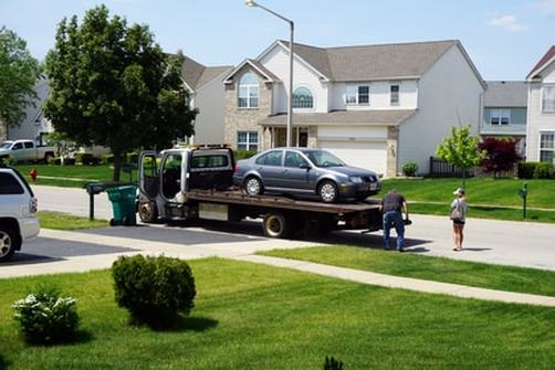 A woman looks on as her car sits on the bed of a flatbed truck.